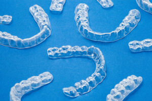 Multiple clear orthodontic aligner trays arranged on a blue background, used for teeth straightening and smile correction.